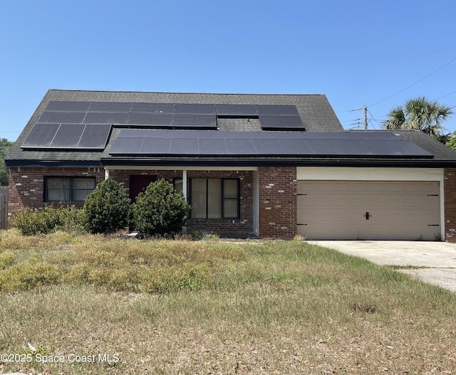 view of front of home with roof mounted solar panels, an attached garage, driveway, and brick siding