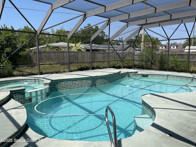 view of swimming pool with fence, a lanai, and a pool with connected hot tub