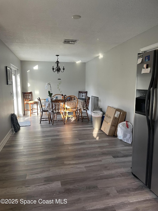 dining room featuring visible vents, a textured ceiling, a chandelier, and dark wood finished floors