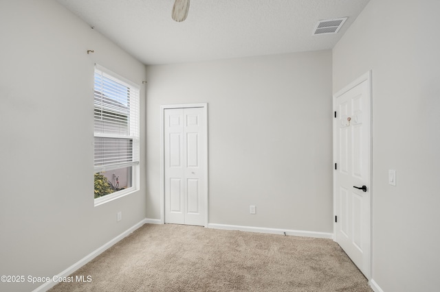 unfurnished bedroom with visible vents, a closet, baseboards, a textured ceiling, and carpet flooring
