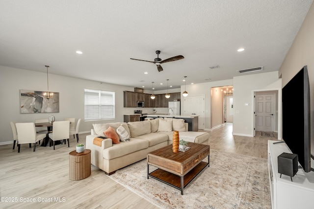 living area with baseboards, visible vents, light wood finished floors, and ceiling fan with notable chandelier