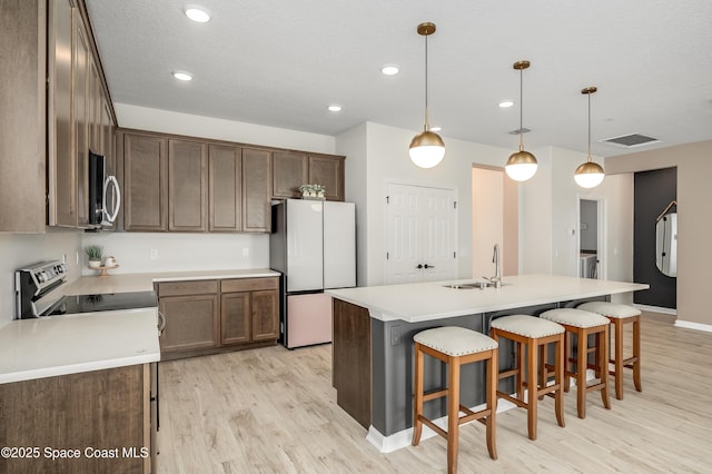 kitchen with appliances with stainless steel finishes, a sink, light wood-style floors, a kitchen breakfast bar, and visible vents