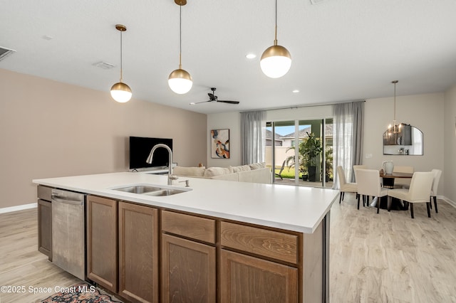kitchen with stainless steel dishwasher, open floor plan, a sink, light wood finished floors, and hanging light fixtures