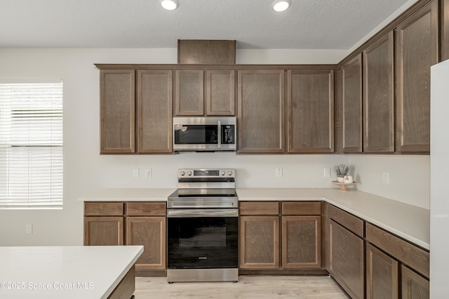kitchen with light wood-type flooring, light countertops, a textured ceiling, and appliances with stainless steel finishes
