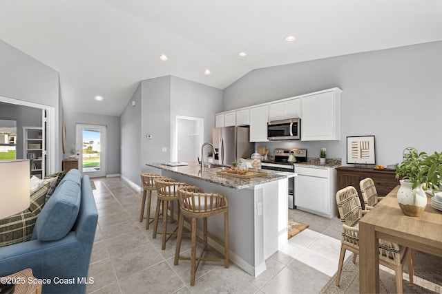kitchen with light stone countertops, light tile patterned floors, appliances with stainless steel finishes, open floor plan, and lofted ceiling