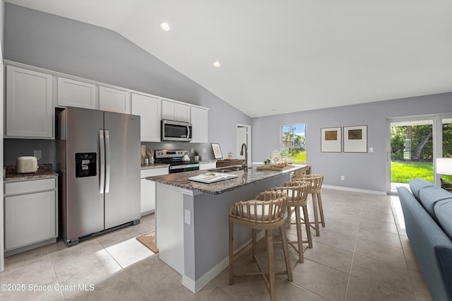 kitchen with lofted ceiling, dark stone countertops, a sink, stainless steel appliances, and an island with sink