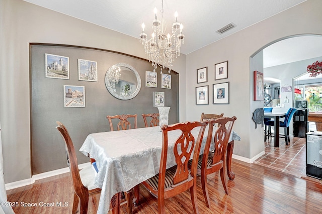dining area with arched walkways, visible vents, a chandelier, and wood finished floors