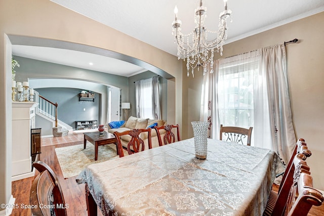 dining area featuring stairway, wood finished floors, a chandelier, and arched walkways