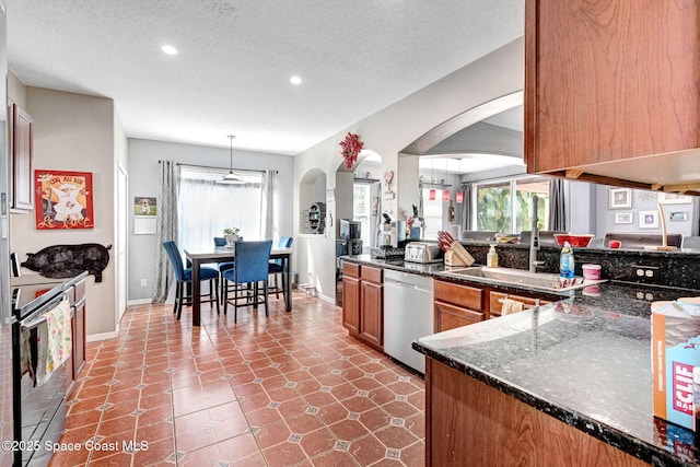 kitchen with a wealth of natural light, brown cabinets, stainless steel appliances, and arched walkways