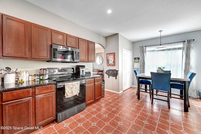 kitchen featuring a textured ceiling, brown cabinets, appliances with stainless steel finishes, baseboards, and arched walkways