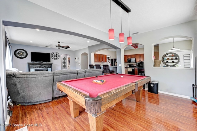 rec room with arched walkways, a fireplace, light wood finished floors, visible vents, and a ceiling fan