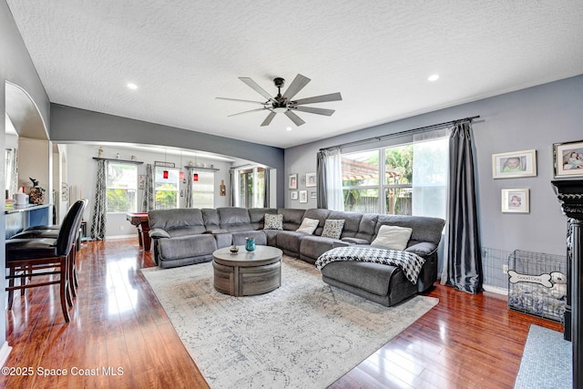 living area featuring a textured ceiling, ceiling fan, wood-type flooring, and arched walkways
