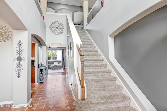stairs featuring tile patterned flooring, arched walkways, baseboards, and a high ceiling