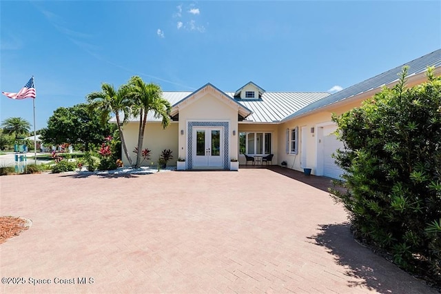 view of front facade with a standing seam roof, decorative driveway, metal roof, a garage, and french doors
