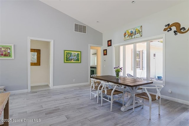 dining room featuring visible vents, baseboards, high vaulted ceiling, and light wood-style floors