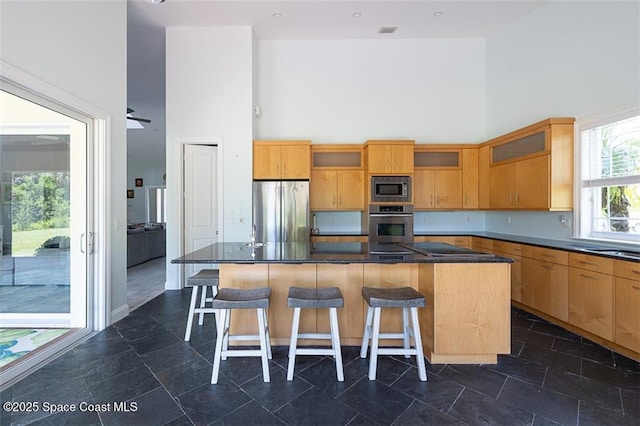 kitchen with glass insert cabinets, a towering ceiling, a kitchen island, and stainless steel appliances