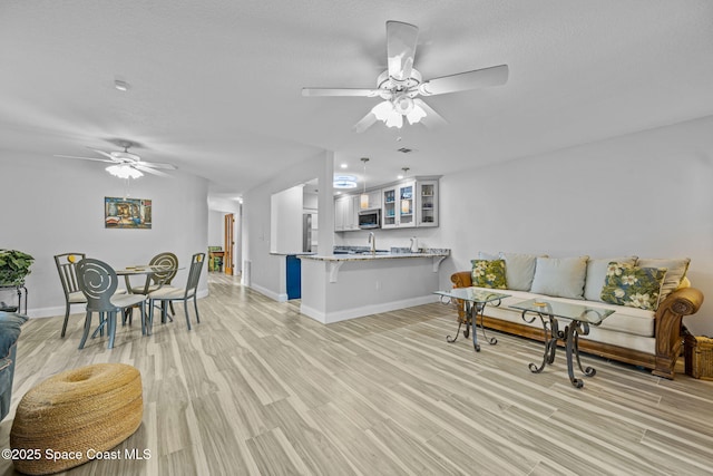 living area with a textured ceiling, ceiling fan, baseboards, and light wood-type flooring