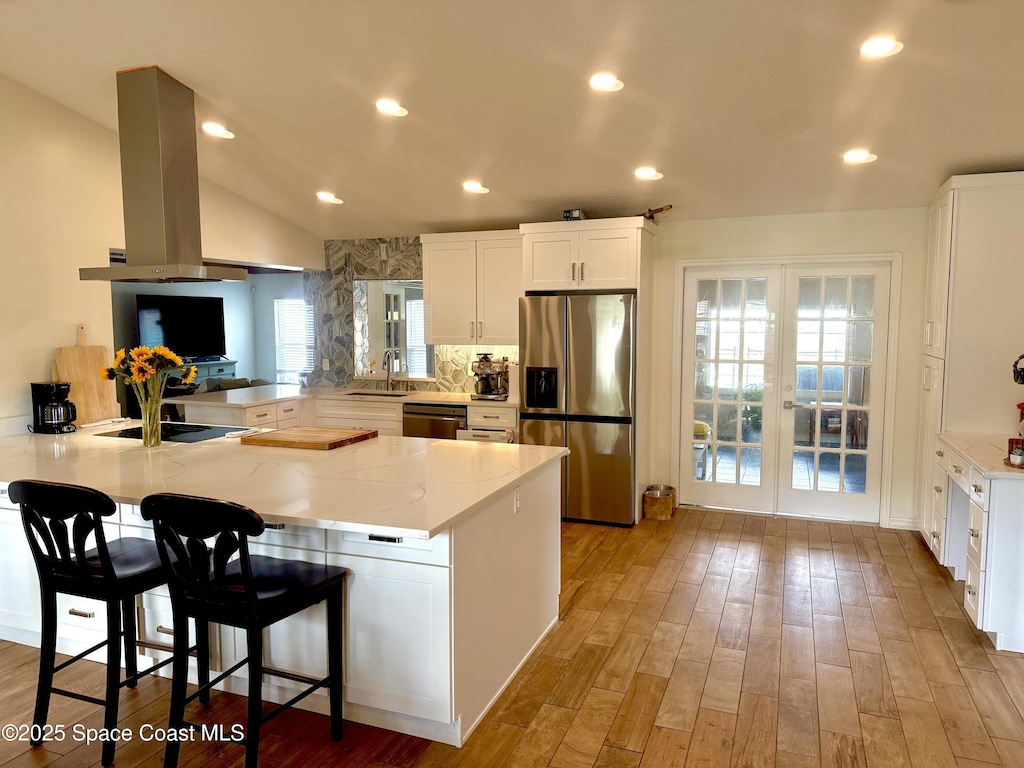 kitchen with light stone counters, stainless steel appliances, island exhaust hood, french doors, and a peninsula