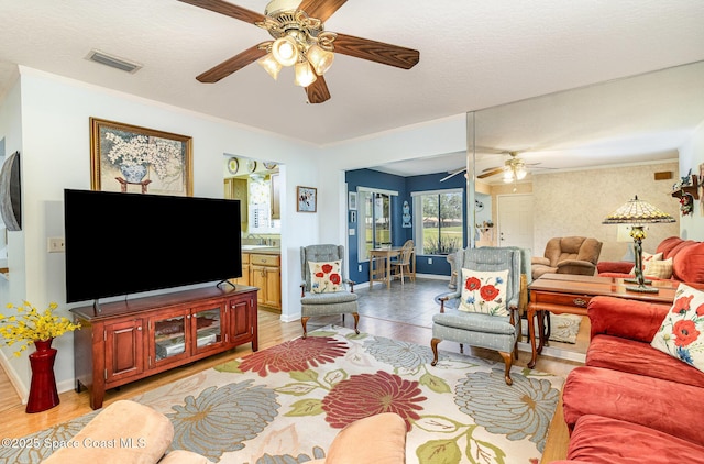 living room featuring ceiling fan, light wood finished floors, baseboards, visible vents, and ornamental molding