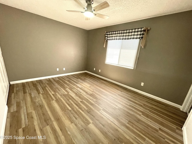 empty room with a textured ceiling, ceiling fan, wood finished floors, and baseboards