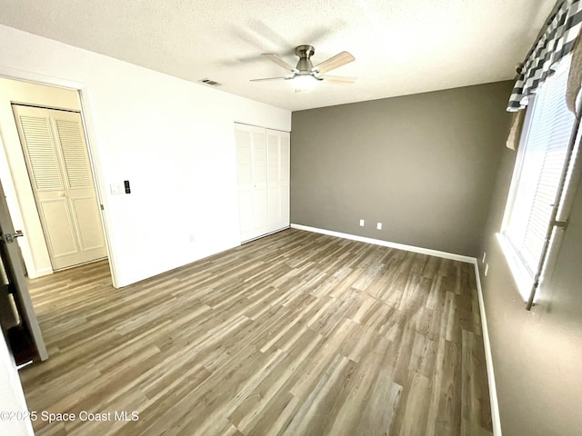 unfurnished bedroom featuring a closet, a ceiling fan, visible vents, baseboards, and wood finished floors