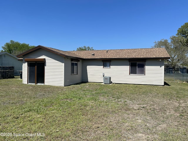 back of property featuring central AC, fence, a shingled roof, and a lawn