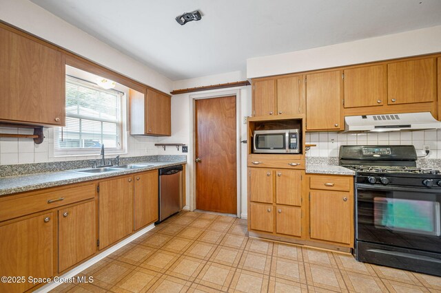 kitchen with backsplash, a sink, under cabinet range hood, light floors, and stainless steel appliances