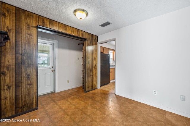 empty room with a textured ceiling, visible vents, wood walls, baseboards, and light floors
