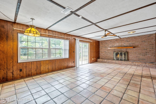 unfurnished living room with a textured ceiling, visible vents, tile patterned flooring, a brick fireplace, and wood walls