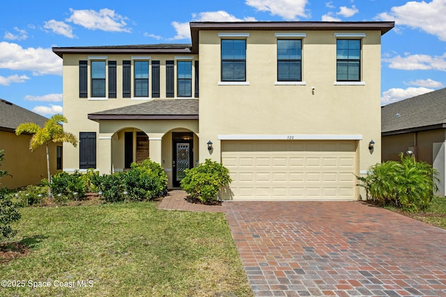 traditional-style house featuring an attached garage, stucco siding, a front lawn, and decorative driveway
