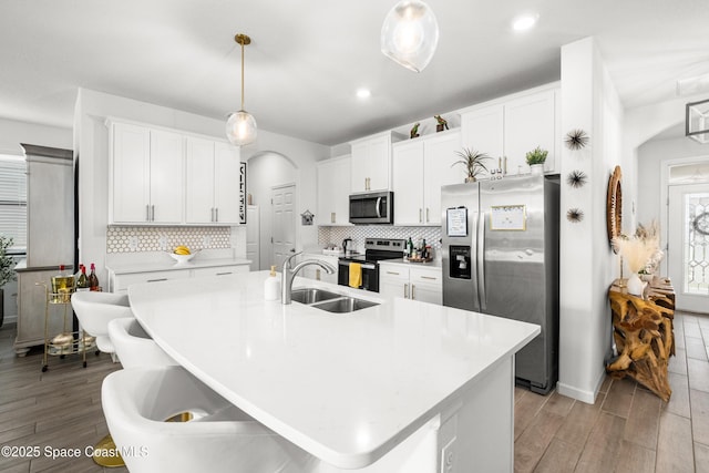 kitchen featuring arched walkways, light wood finished floors, stainless steel appliances, and a sink