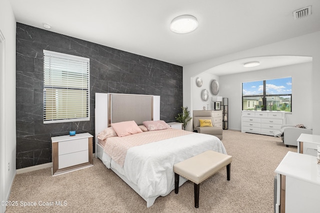 bedroom featuring tile walls, an accent wall, visible vents, and light colored carpet