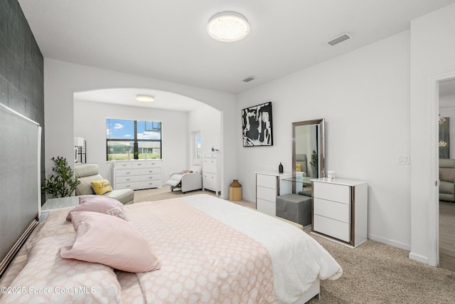 bedroom featuring light carpet, arched walkways, baseboards, and visible vents
