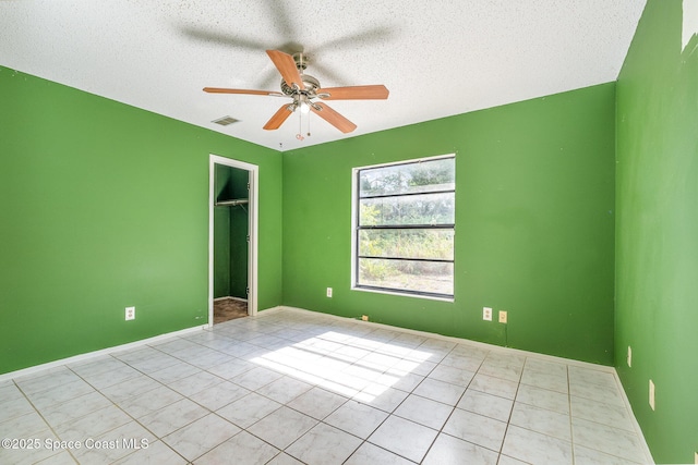 unfurnished bedroom featuring tile patterned floors, a ceiling fan, a closet, a textured ceiling, and a walk in closet