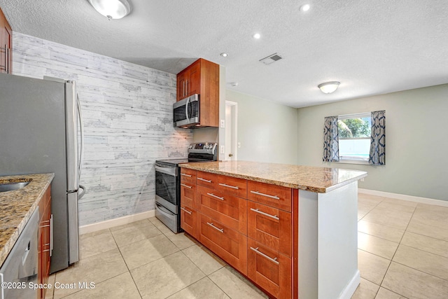 kitchen with baseboards, a peninsula, appliances with stainless steel finishes, and an accent wall