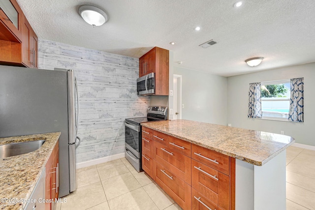 kitchen featuring a textured ceiling, baseboards, a peninsula, an accent wall, and stainless steel appliances