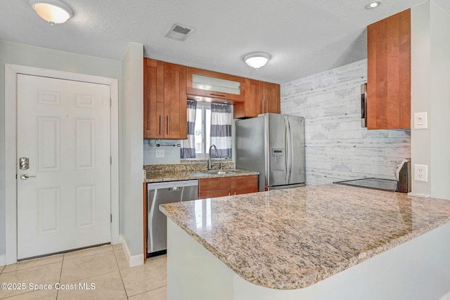 kitchen with a peninsula, light stone countertops, brown cabinets, a sink, and appliances with stainless steel finishes