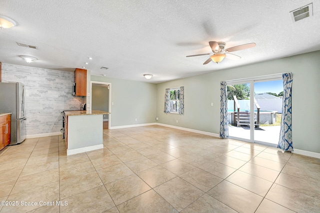 unfurnished living room with visible vents, baseboards, ceiling fan, and an accent wall