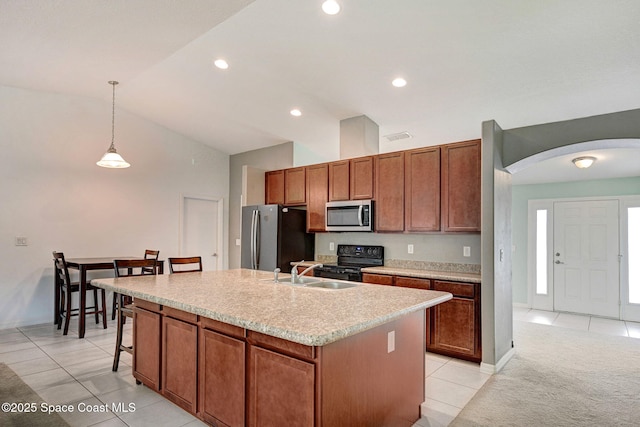 kitchen with light tile patterned floors, a sink, stainless steel appliances, a kitchen island with sink, and arched walkways