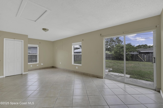 empty room with baseboards, a textured ceiling, and light tile patterned floors