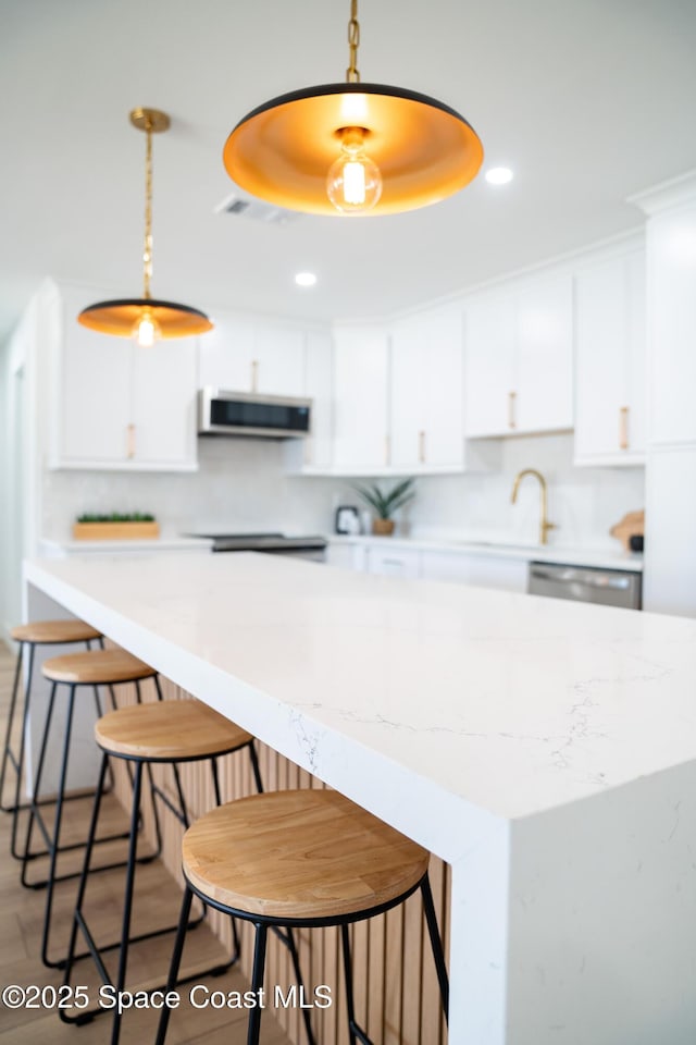 kitchen featuring backsplash, white cabinets, appliances with stainless steel finishes, and decorative light fixtures