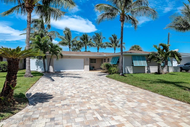 single story home with decorative driveway, a garage, a front lawn, and stucco siding