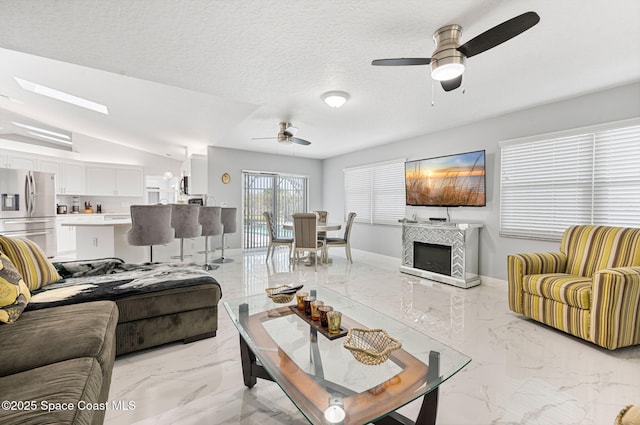 living area featuring ceiling fan, a fireplace, a textured ceiling, marble finish floor, and lofted ceiling
