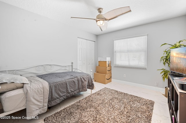 bedroom with a closet, a ceiling fan, marble finish floor, and baseboards