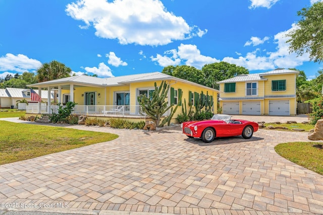 view of front of house featuring an attached garage, a front yard, decorative driveway, covered porch, and metal roof