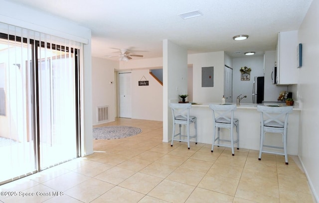 kitchen featuring visible vents, freestanding refrigerator, a kitchen breakfast bar, electric panel, and a ceiling fan