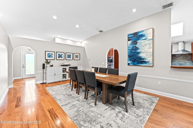 dining area featuring light wood-style floors, arched walkways, and recessed lighting