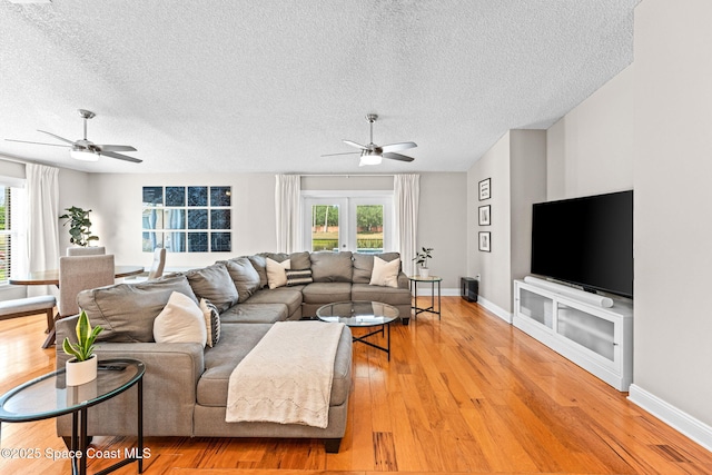 living room with a textured ceiling, ceiling fan, baseboards, and light wood-style floors