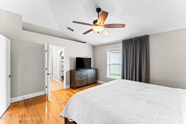 bedroom featuring ceiling fan, a textured ceiling, light wood-style flooring, vaulted ceiling, and visible vents