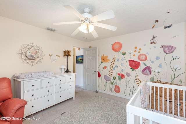 bedroom with ceiling fan, visible vents, light colored carpet, a crib, and baseboards